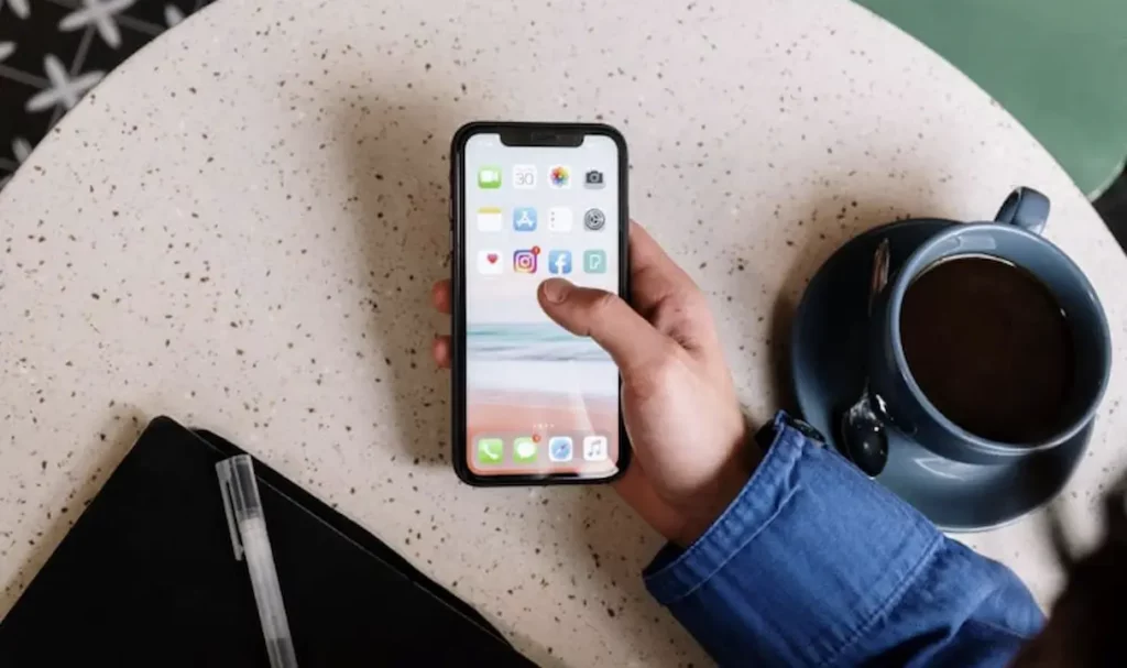شخص يحمل هاتفًا ذكيًا يعرض تطبيقات مثل instagram