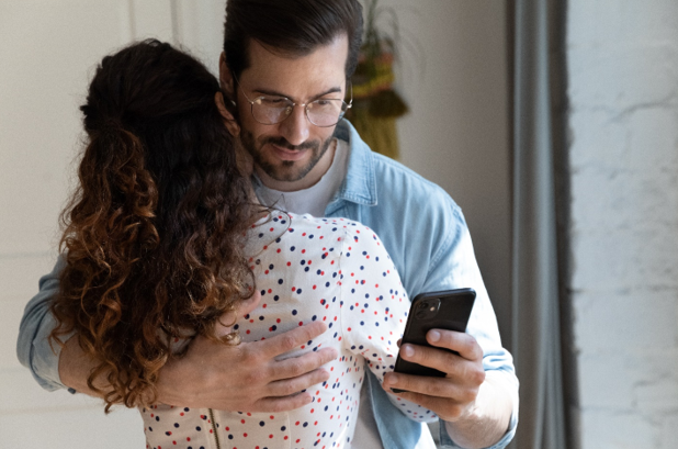 esposo abrazando a su esposa y mirando el teléfono