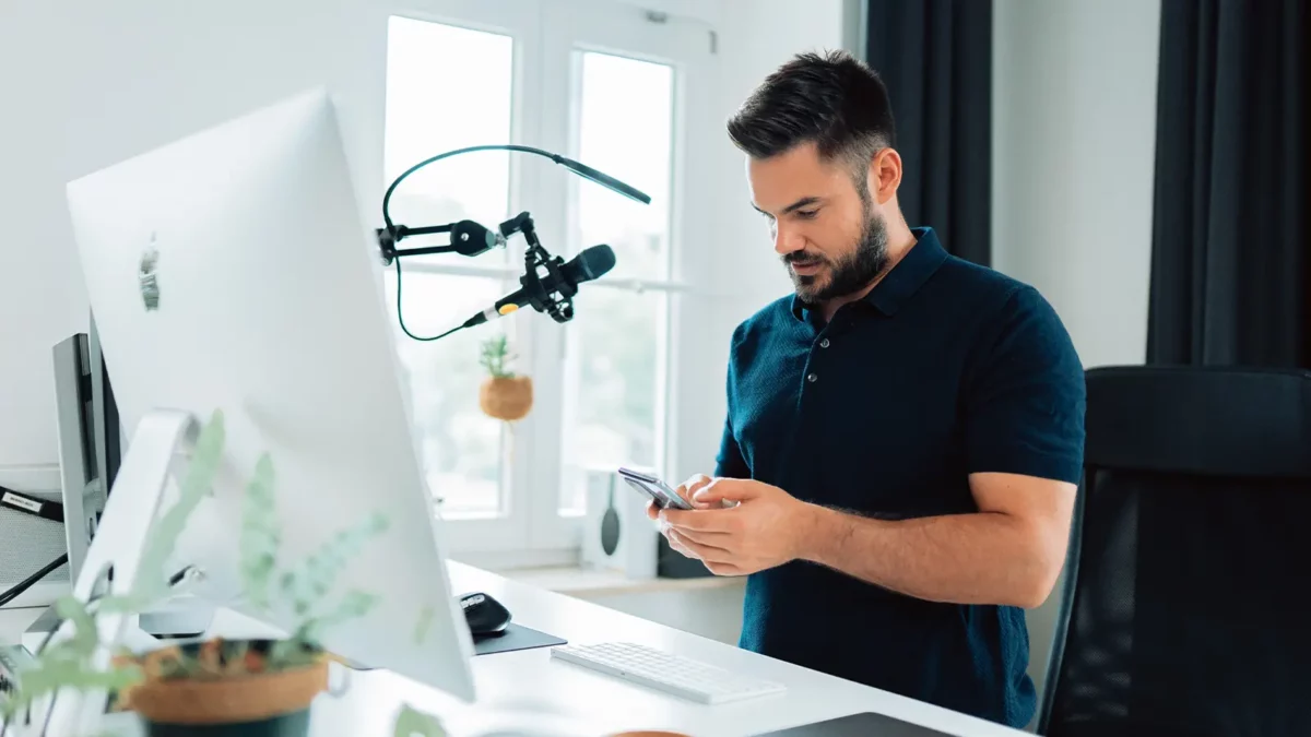 Mann vor einem Mikrofon, der durch sein Telefon schaut