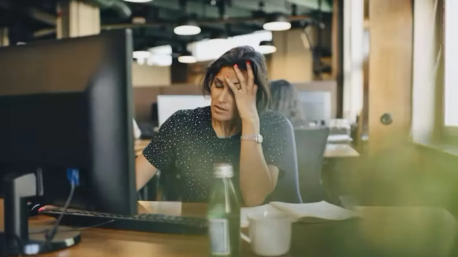 mulher em sua mesa no trabalho segurando sua cabeça