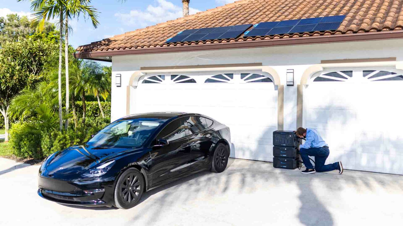 Un automóvil mediano de lujo en un camino de entrada junto a una central eléctrica BLUETTI y paneles solares