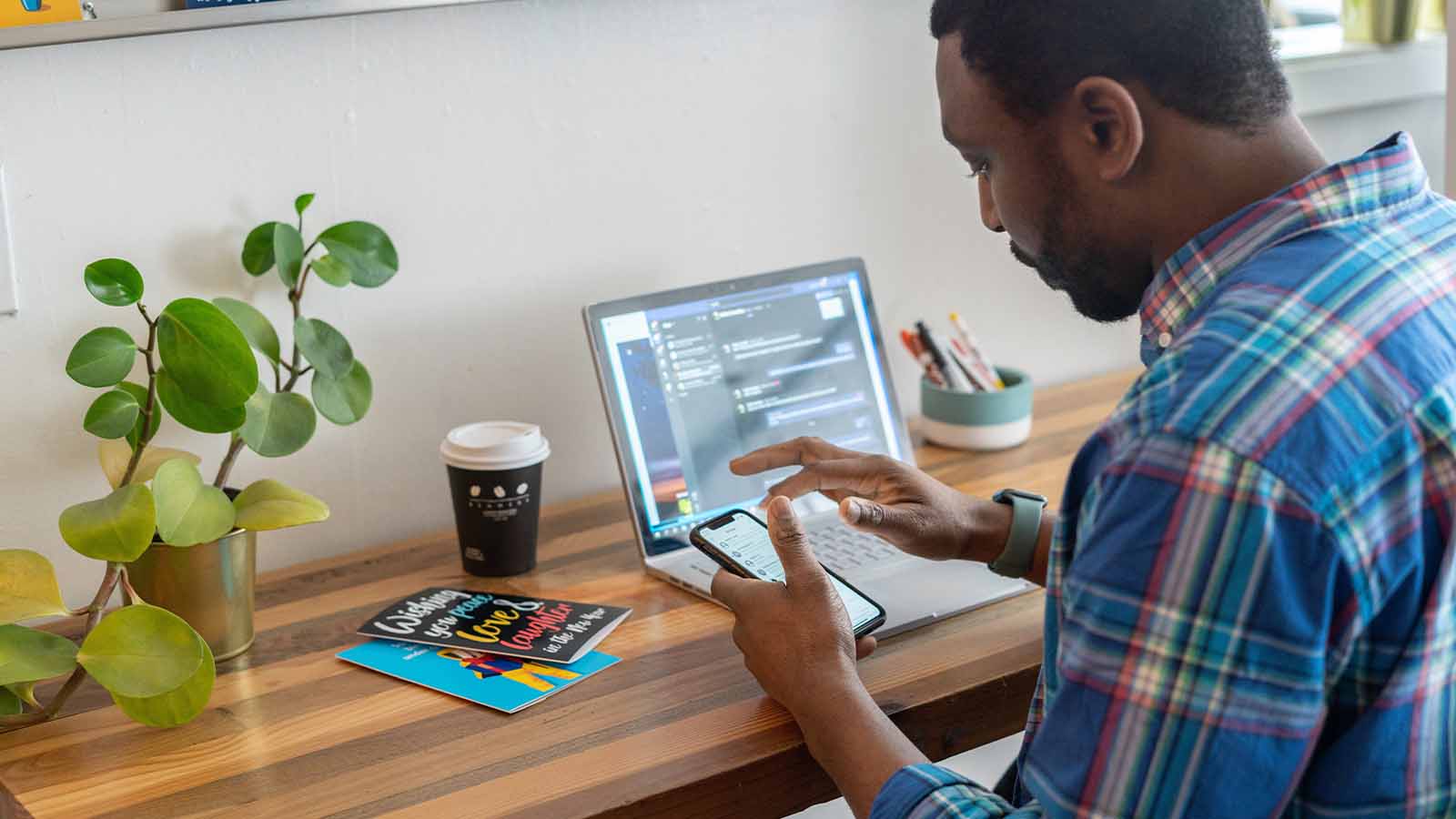 homem olhando para o telefone na frente de seu computador