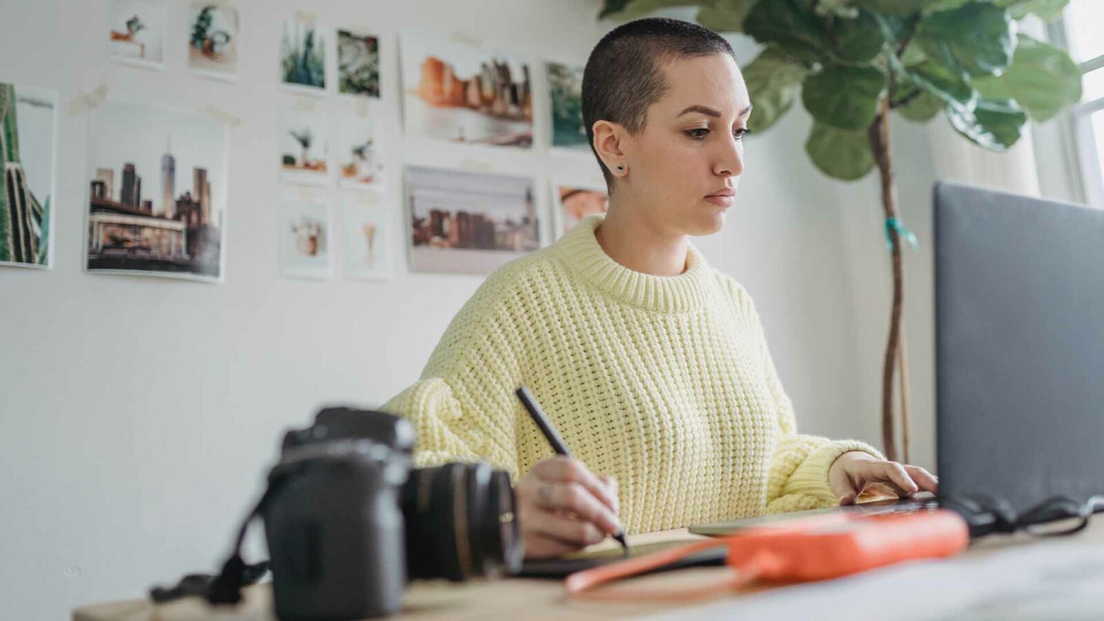 Uma pessoa está sentada em uma mesa em um prédio de escritórios, usando um computador e cercada por móveis, materiais de escritório e uma mesa.