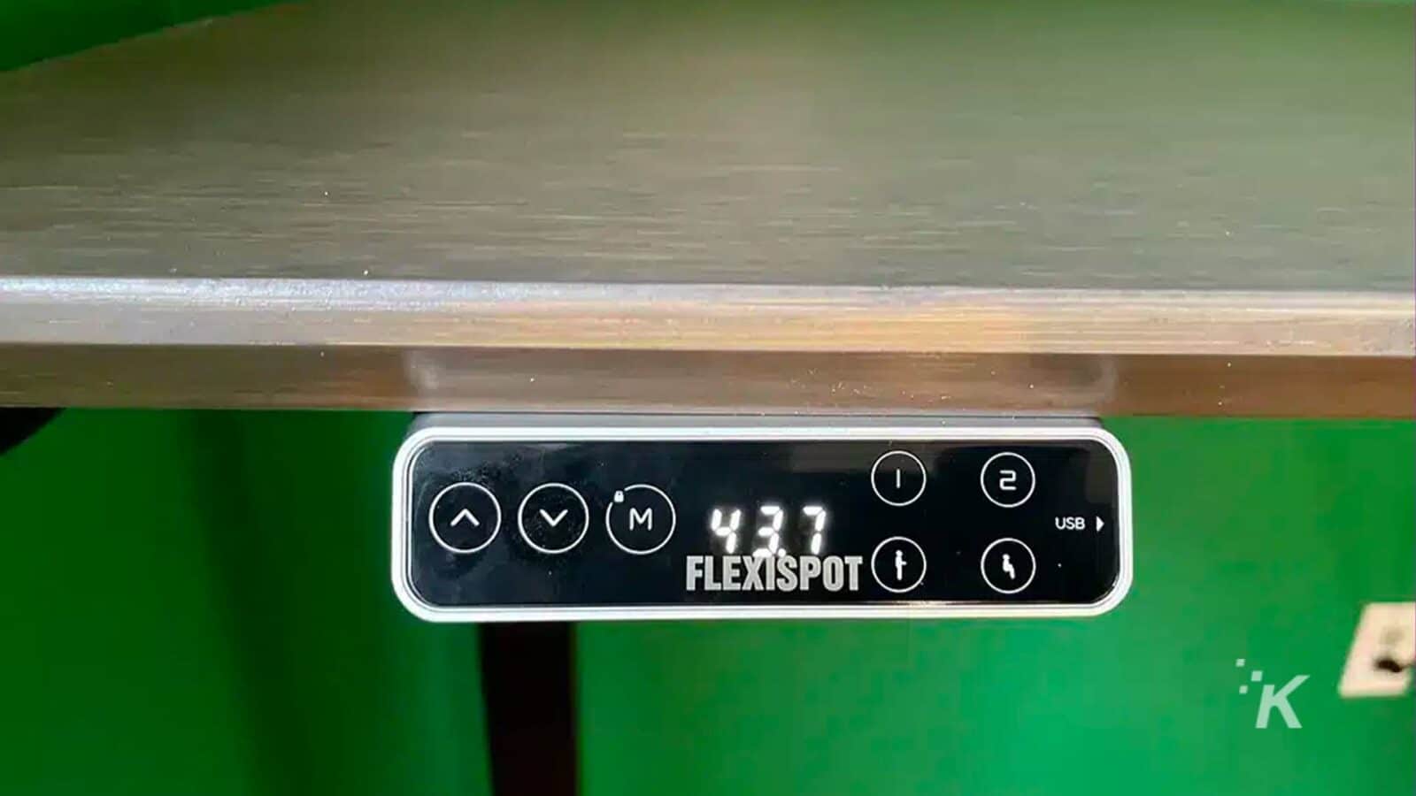 La imagen muestra un cable USB conectado a un dispositivo FlexiSpot. Texto completo: - VM) 437 2 1 USB de FLEXISPOT K