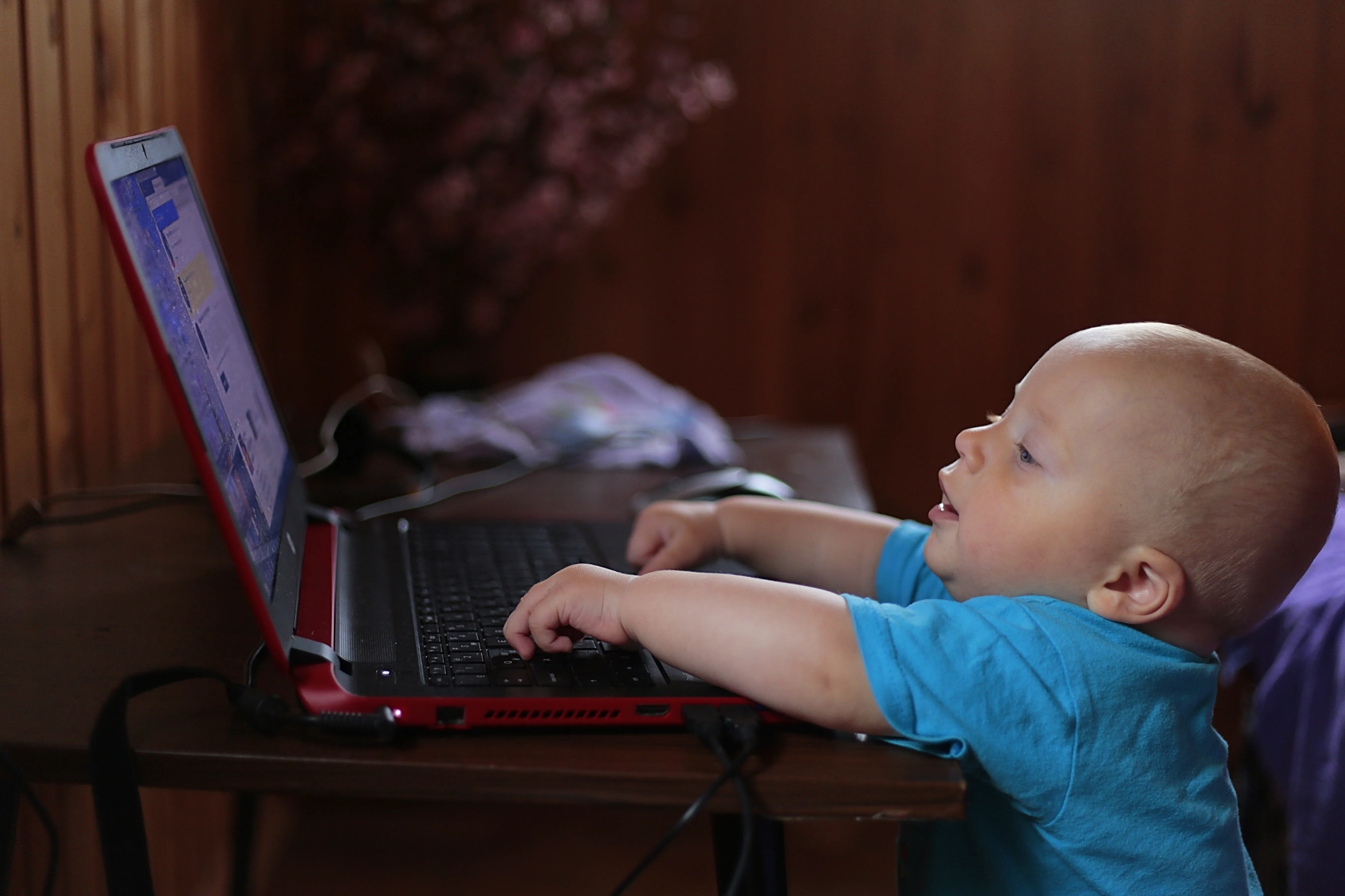 Niño con camiseta azul usando una computadora portátil negra en un escenario con poca luz