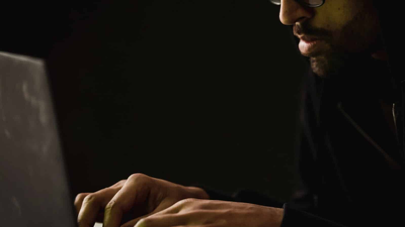 Persona en un entorno oscuro escribiendo en una computadora portátil en la web oscura
