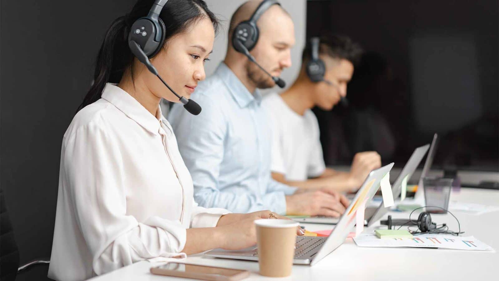 Une personne portant des écouteurs écoute attentivement son ordinateur alors qu'elle est assise à son bureau dans un lieu de travail intérieur.