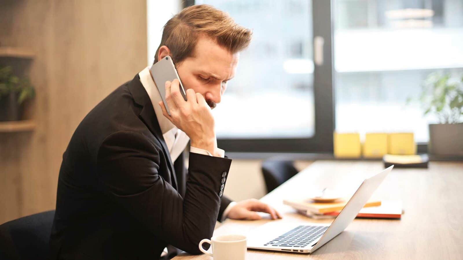 Une personne reçoit des appels automatisés au téléphone et travaille sur un ordinateur portable.