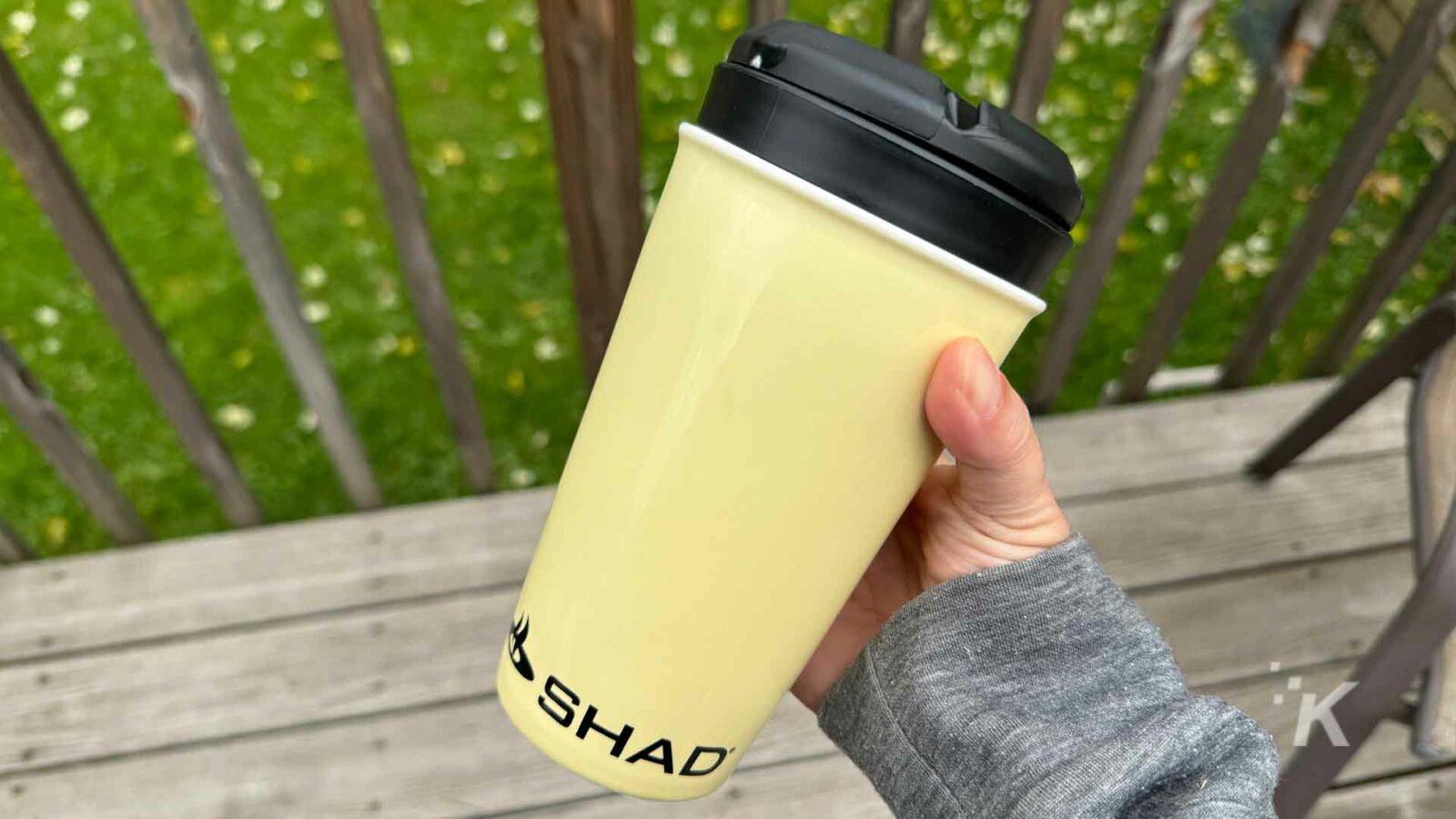 A person is enjoying a cup of coffee outdoors with a yellow paper cup and tableware.