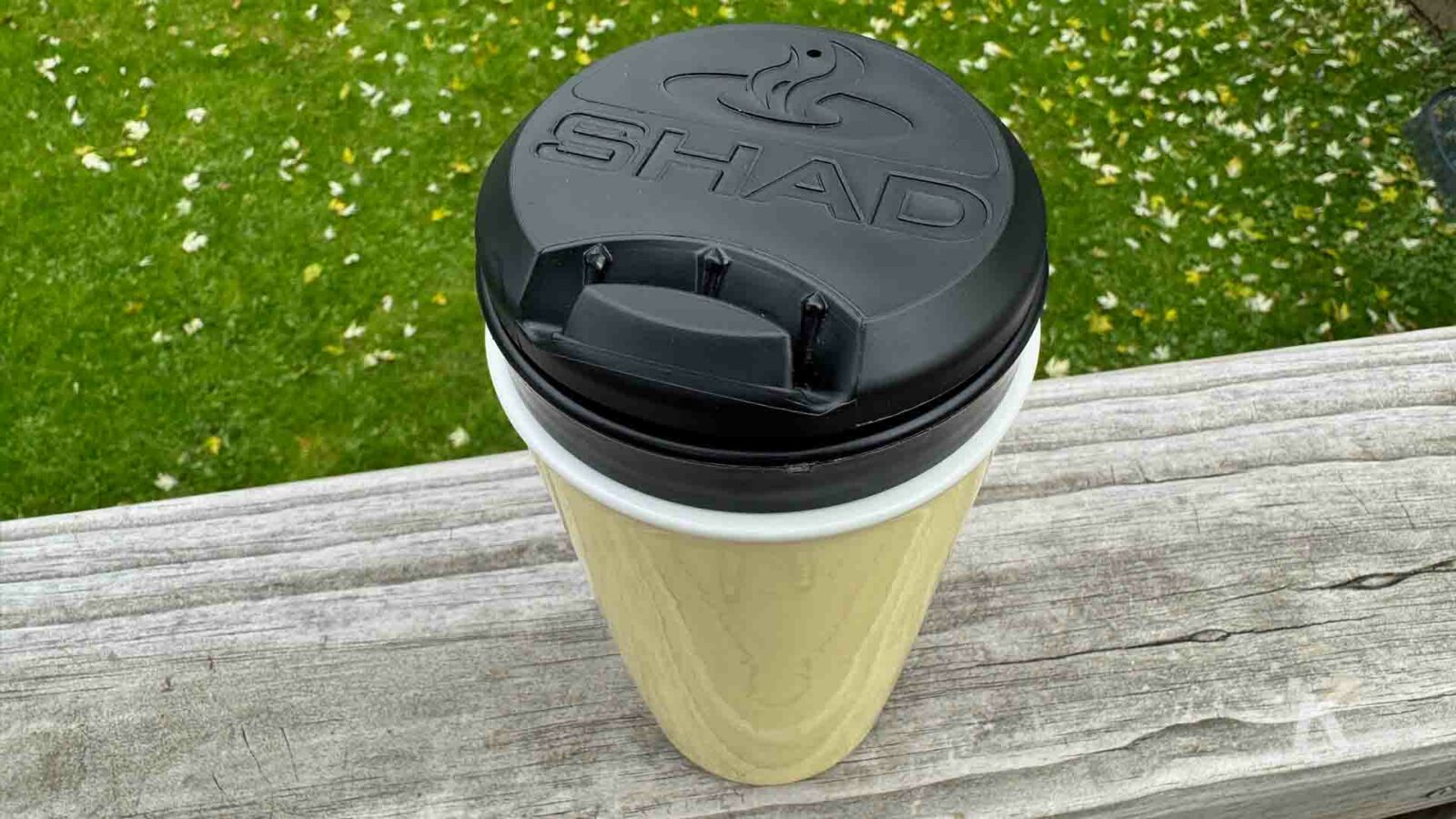 Un grupo de personas está sentada en el césped disfrutando de un café en vasos de papel, con la vajilla y los vasos con tapa colocados en un contenedor de basura cercano.