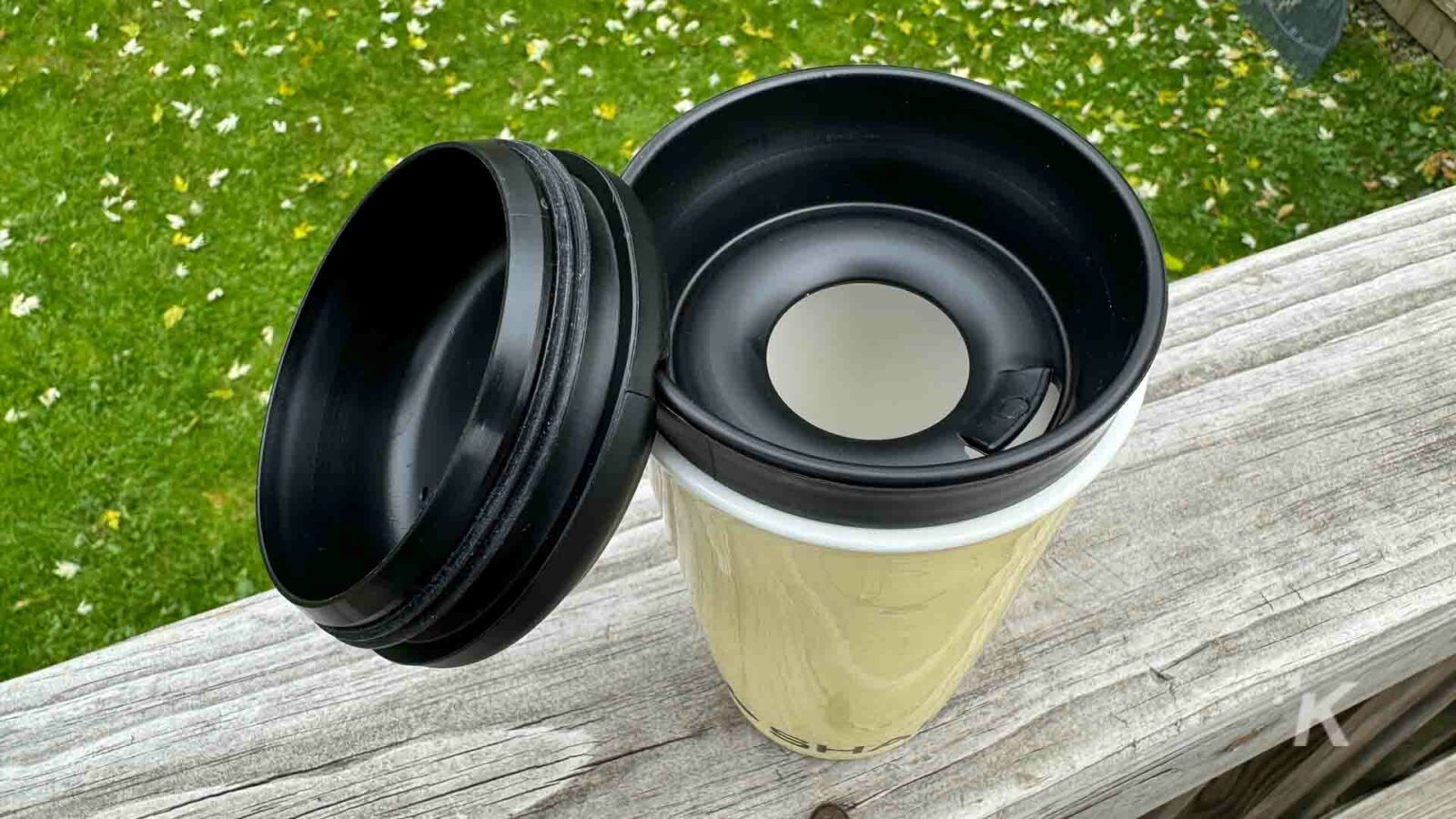 Una vajilla de madera con una taza de café se encuentra sobre una superficie cubierta de hierba al aire libre.