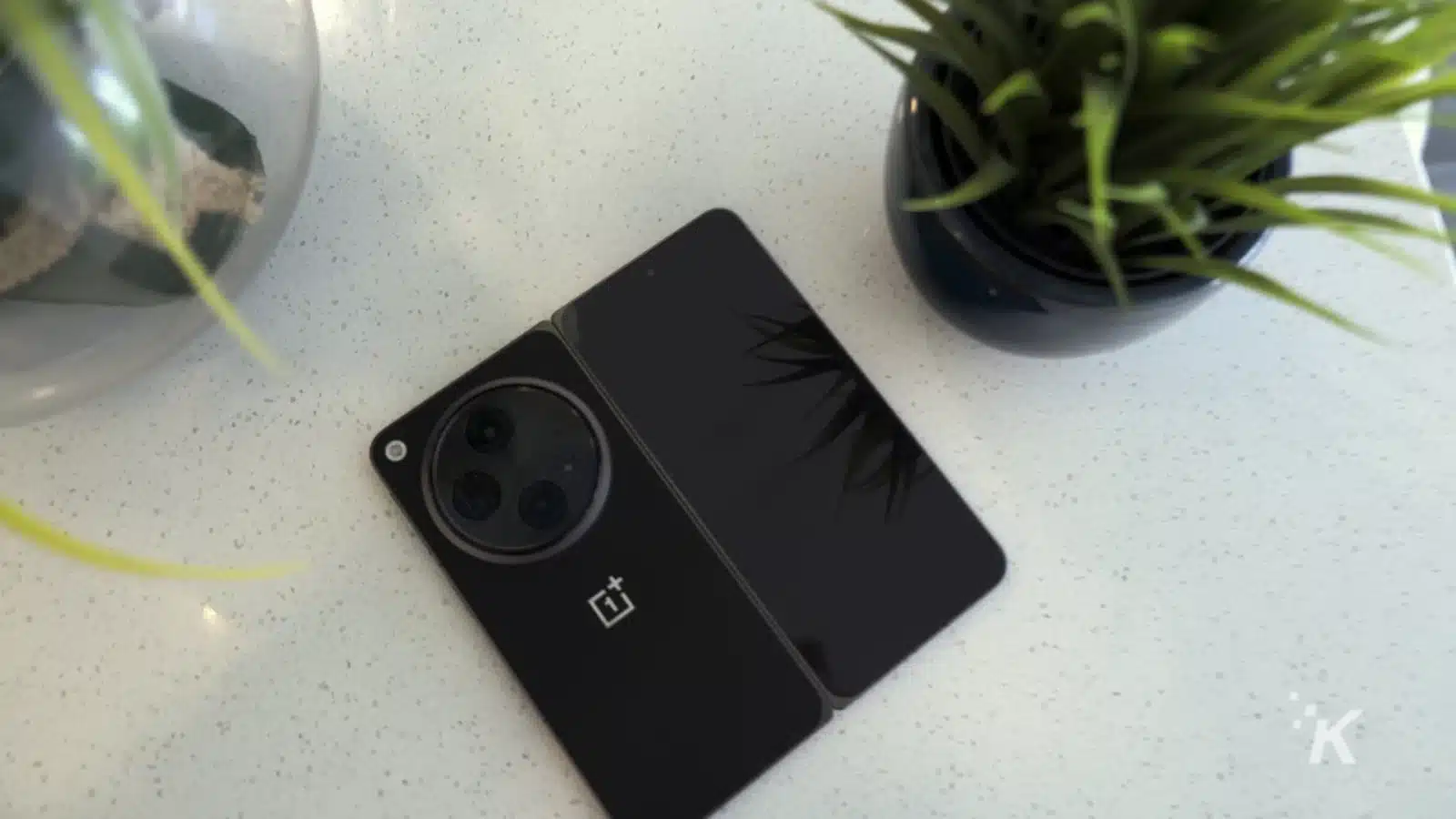 A houseplant blooms in a flowerpot next to a gadget and mobile phone on an indoor table.