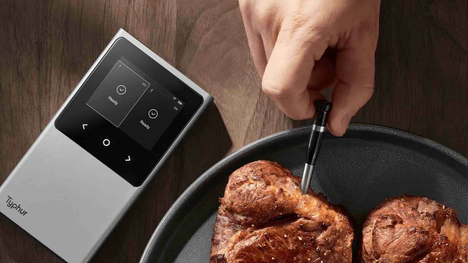 L'image montre une main utilisant un thermomètre à viande numérique pour vérifier la température de deux steaks cuisant dans une poêle noire, sur un fond en bois.