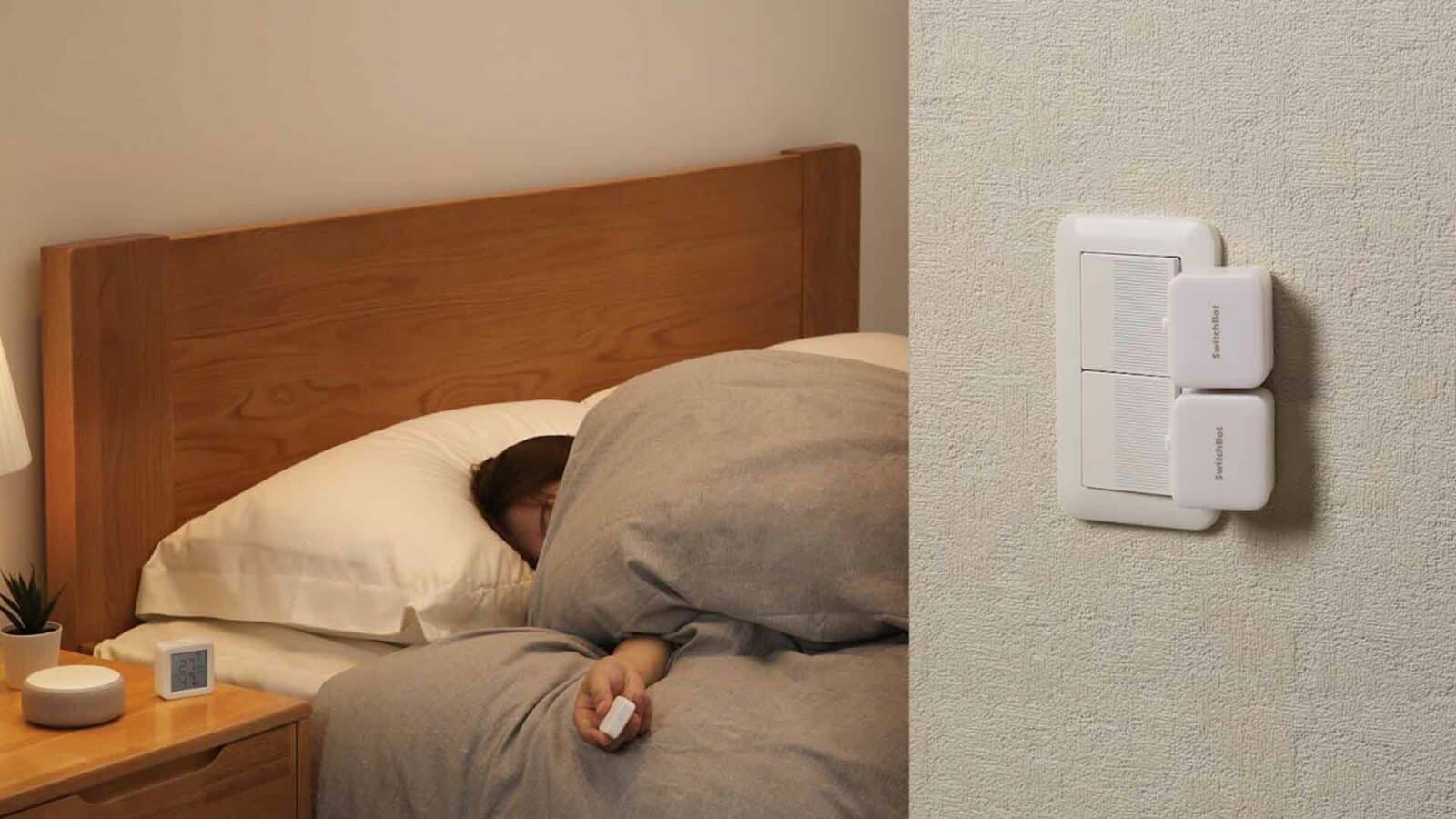 Eine Person liegt im Bett, bedeckt mit grauer Bettwäsche. Rechts ist ein intelligenter Schalter an einer Wand montiert. Die Szene suggeriert moderne Hausautomation.