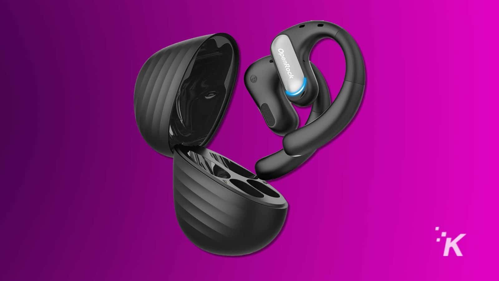 Gli auricolari wireless neri con ganci ergonomici emergono da una custodia di ricarica abbinata su uno sfondo viola vibrante. Sembrano eleganti e moderni. Cuffie Openrock Pro