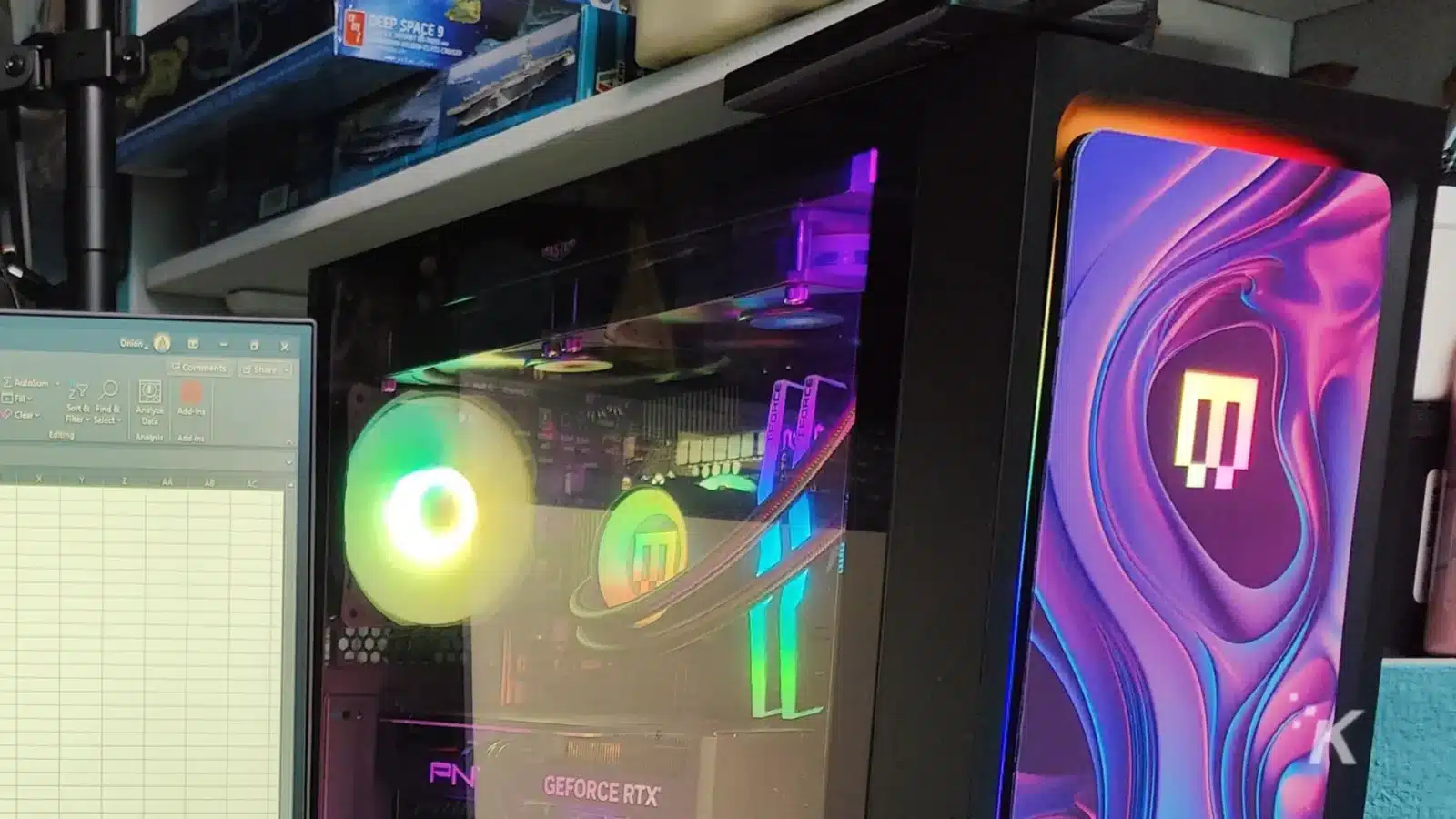 A desktop pc with rgb lighting visible through a clear side panel, featuring a geforce rtx graphics card, beside a monitor with colorful wallpaper.