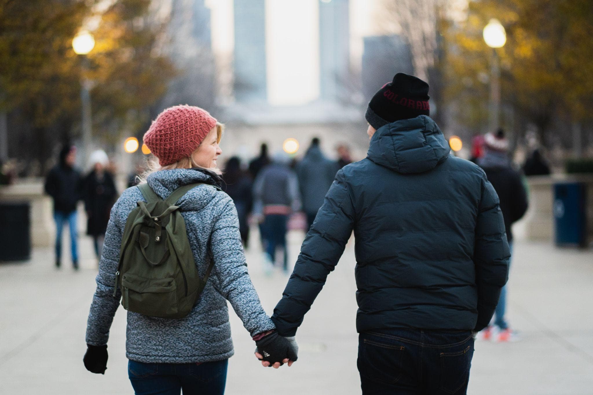 ชายและหญิงจับมือกันสวมเสื้อผ้ากันหนาวขณะเดินไปตามถนน