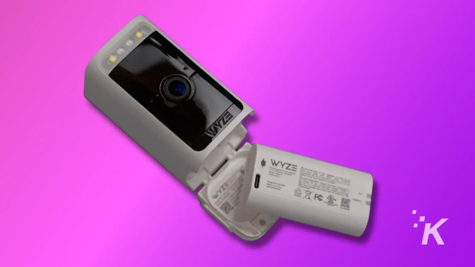 An open wyze security camera lying on a pink surface, showing its lens and internals with led lights, against a purple background.