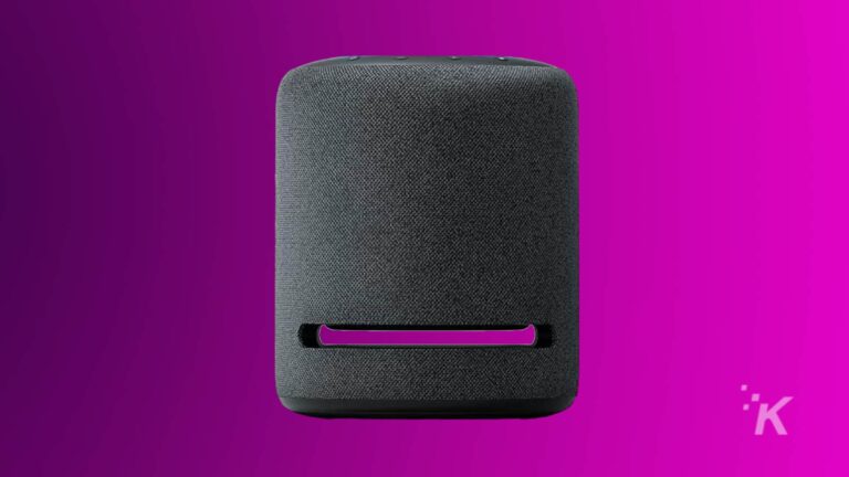 Un altavoz inteligente gris con una funda de tela sobre un fondo morado.