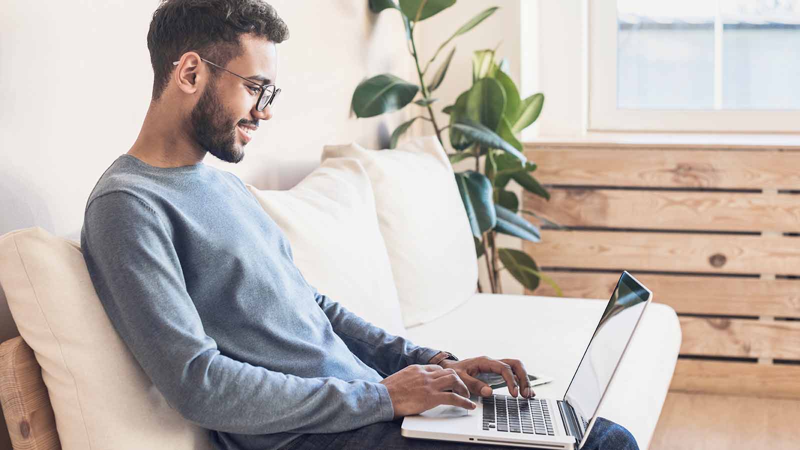 Homme assis sur le canapé en utilisant son ordinateur portable.