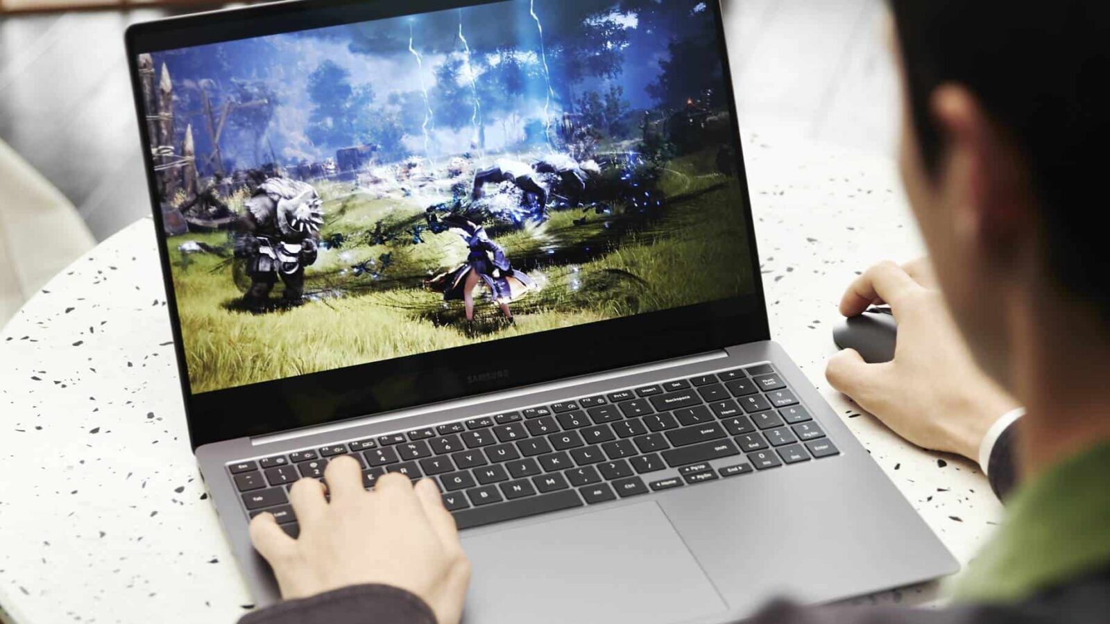 Orang yang memainkan video game fantasi di laptop, menampilkan karakter yang menggunakan sihir melawan monster di layar.