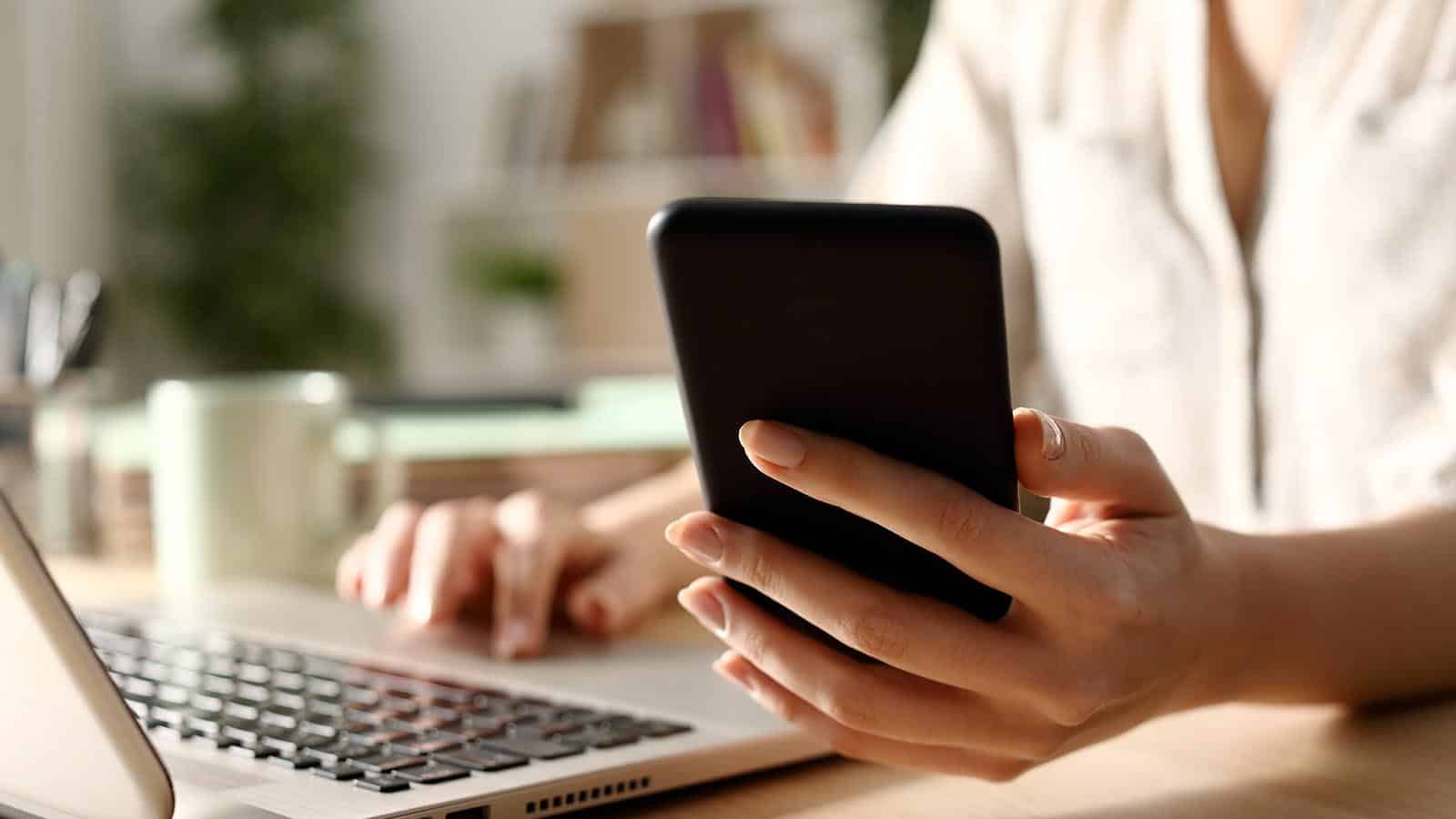 Persona hablando por teléfono frente a una computadora portátil