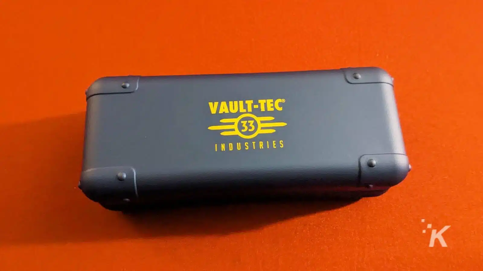 橙色背景上帶有 Vault-Tec 品牌標誌的外殼。