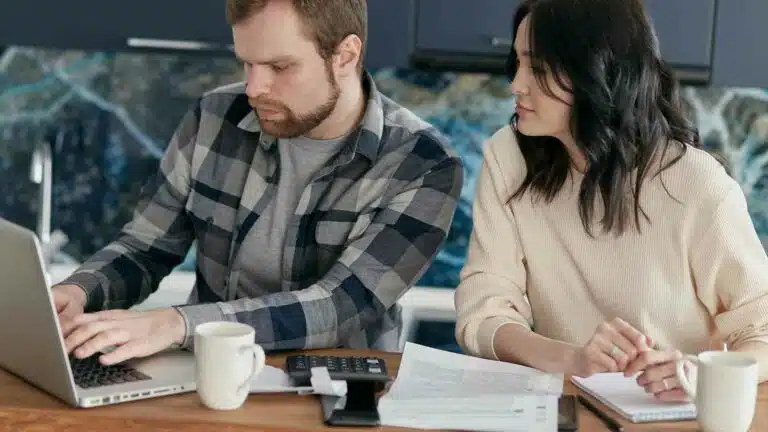 Dois profissionais colaborando em um laptop na mesa do escritório.