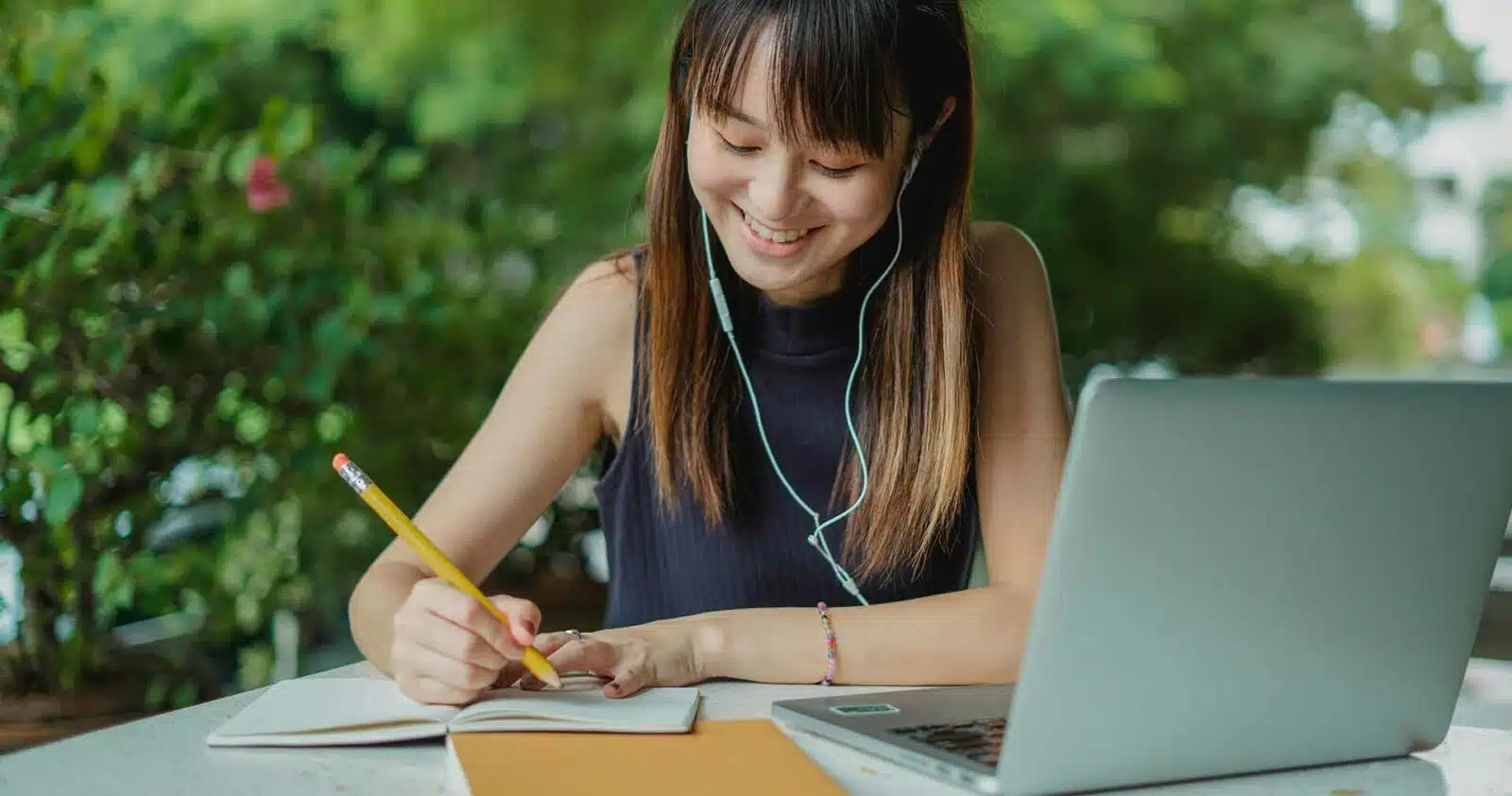 mulher escrevendo no bloco de notas com um laptop ao lado dela.