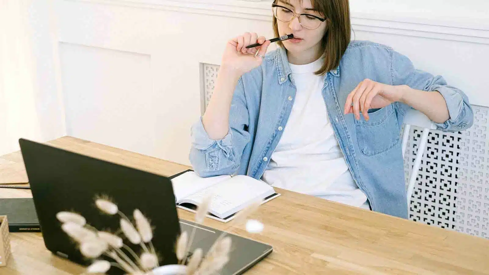 Eine Person sitzt am Tisch vor einem Laptop.