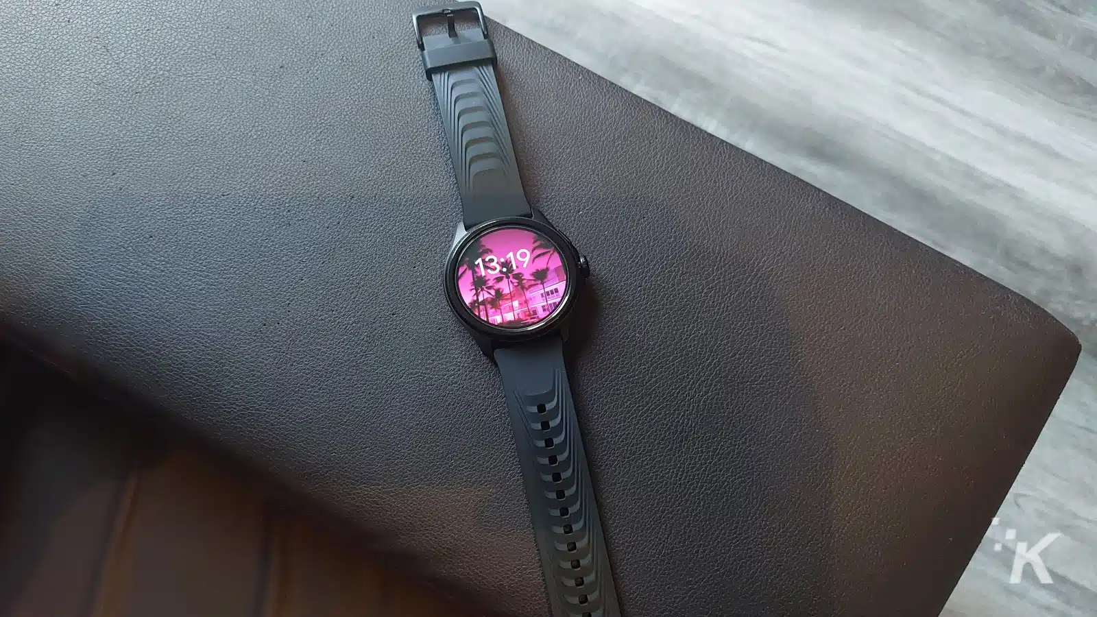 Smartwatch nero con carta da parati di palma su superficie marrone.