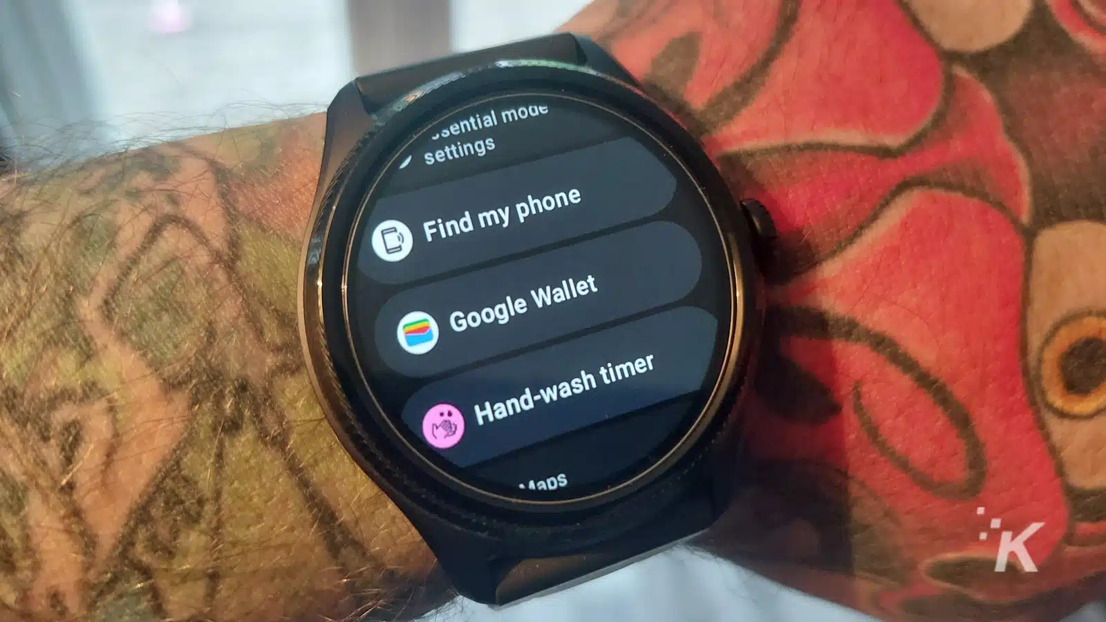 Smartwatch che mostra Google Wallet e app sul polso tatuato.