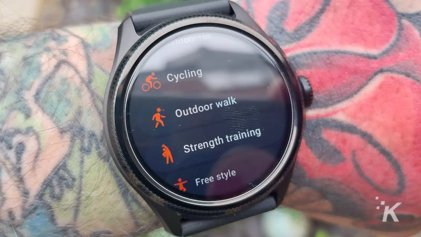 Smartwatch con opzioni di monitoraggio del fitness sul polso tatuato.