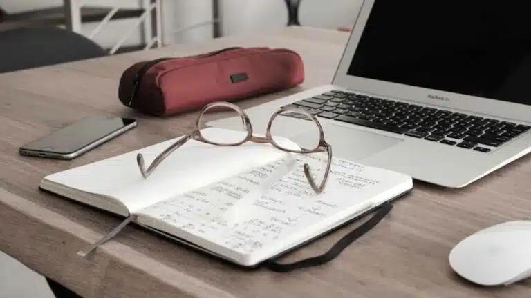 Escritorio de trabajo con computadora portátil, libreta y gafas.