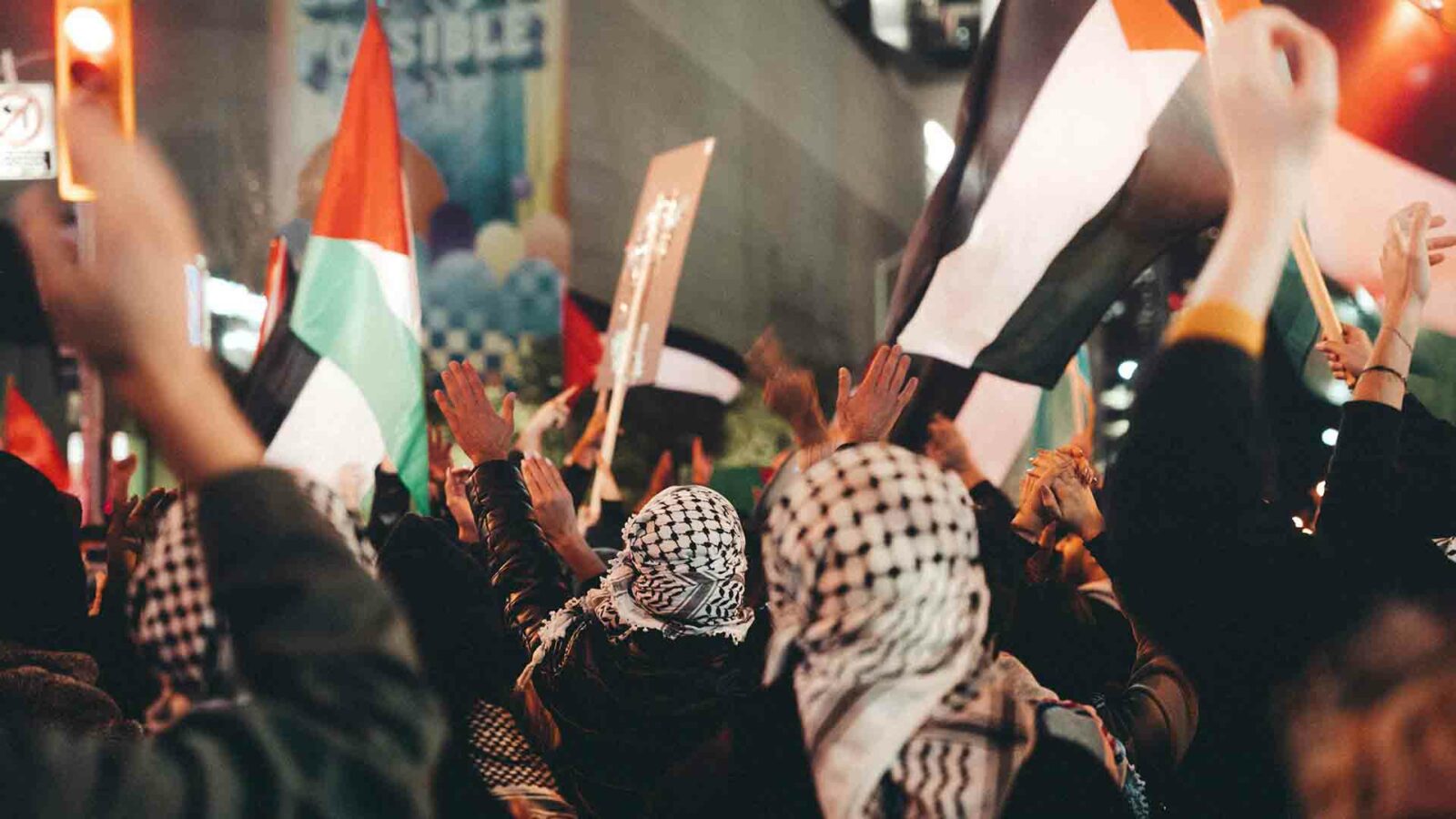 夜の混雑した通りでパレスチナ国旗を掲げた抗議者。
