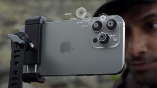 IPhone 15 Pro Max pada tripod dengan seorang pria melihat melalui layar