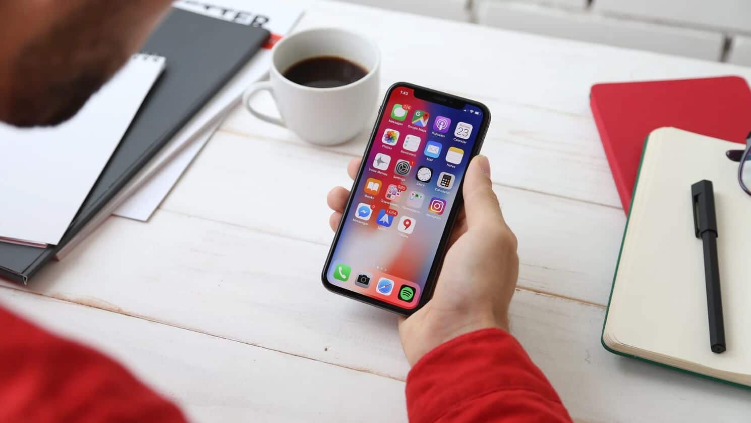 persona sosteniendo un teléfono en un escritorio con una taza de café desarrollo de aplicaciones